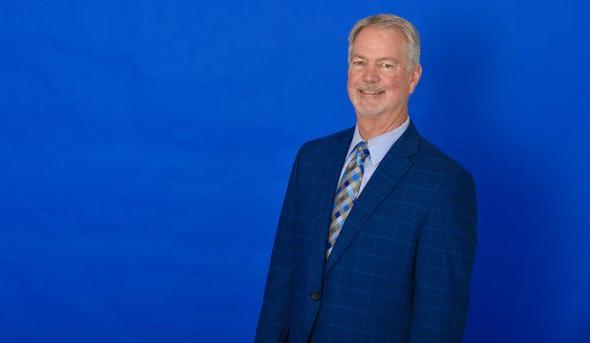 Horizontal headshot of a man against a blue background.